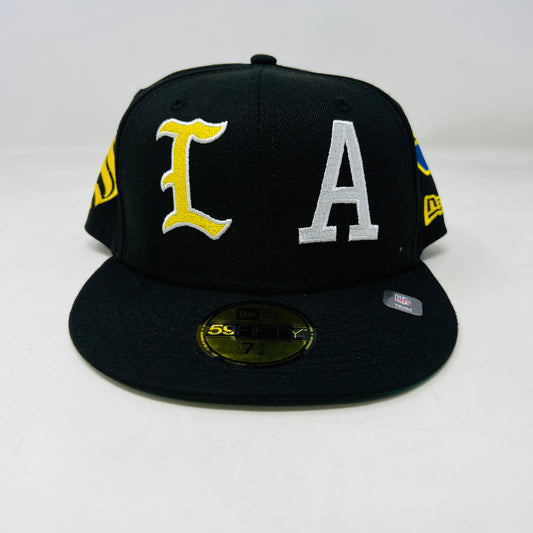 The New Era x Born x Raised x LA RAMS baseball cap by born x raised features LA in yellow and white embroidery on the front. It has a size 7 1/2 sticker on the brim with yellow and blue side patches, all set against a plain white background for a bold statement.