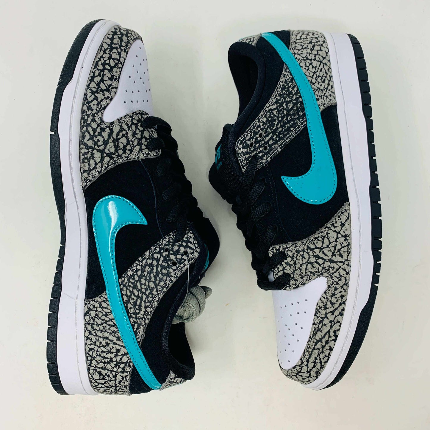 The Nike SB Dunk Low atmos Elephant sneakers feature a black and white textured pattern, teal Nike swoosh, and black laces, displayed on a purple Nike SB box with a white swoosh logo, ensuring 100% authenticity.