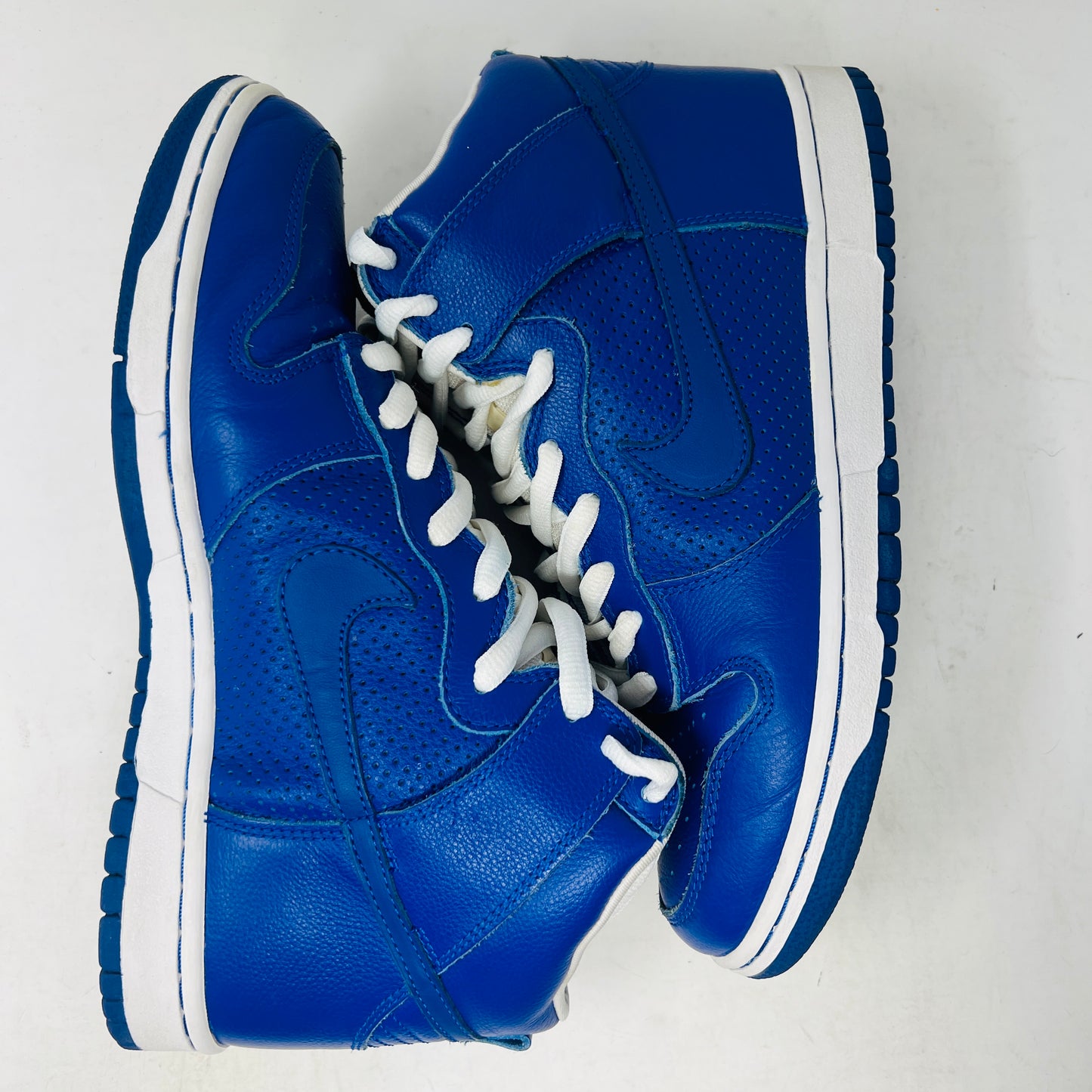 A Nike SB Dunk High T19 Royal Blue sneaker with white laces is perched on a pristine pink shoebox, showcasing the iconic Nike swoosh. The box, in excellent condition, displays a size 10 label.