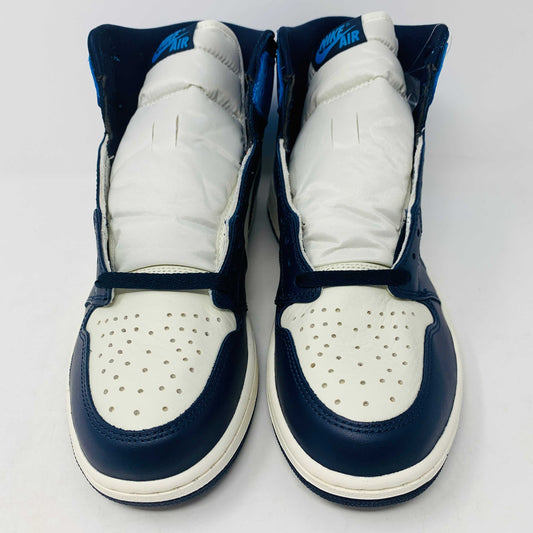 The new Jordan 1 Obsidian high-top sneaker, in blue and white with a black swoosh and blue laces, is displayed on a black and red box featuring 1985 Air Jordan 1 text. A printed Air Jordan wings logo is near the ankle.
