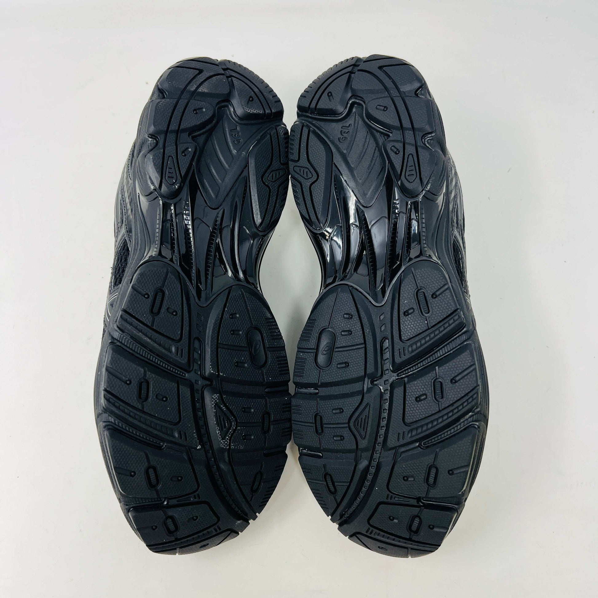 The new ASICS GT-2160 JJJJound Black running shoe sits on its box, featuring extra laces in a clear bag. These authentic shoes present a sleek design with gray detailing and a side text label.