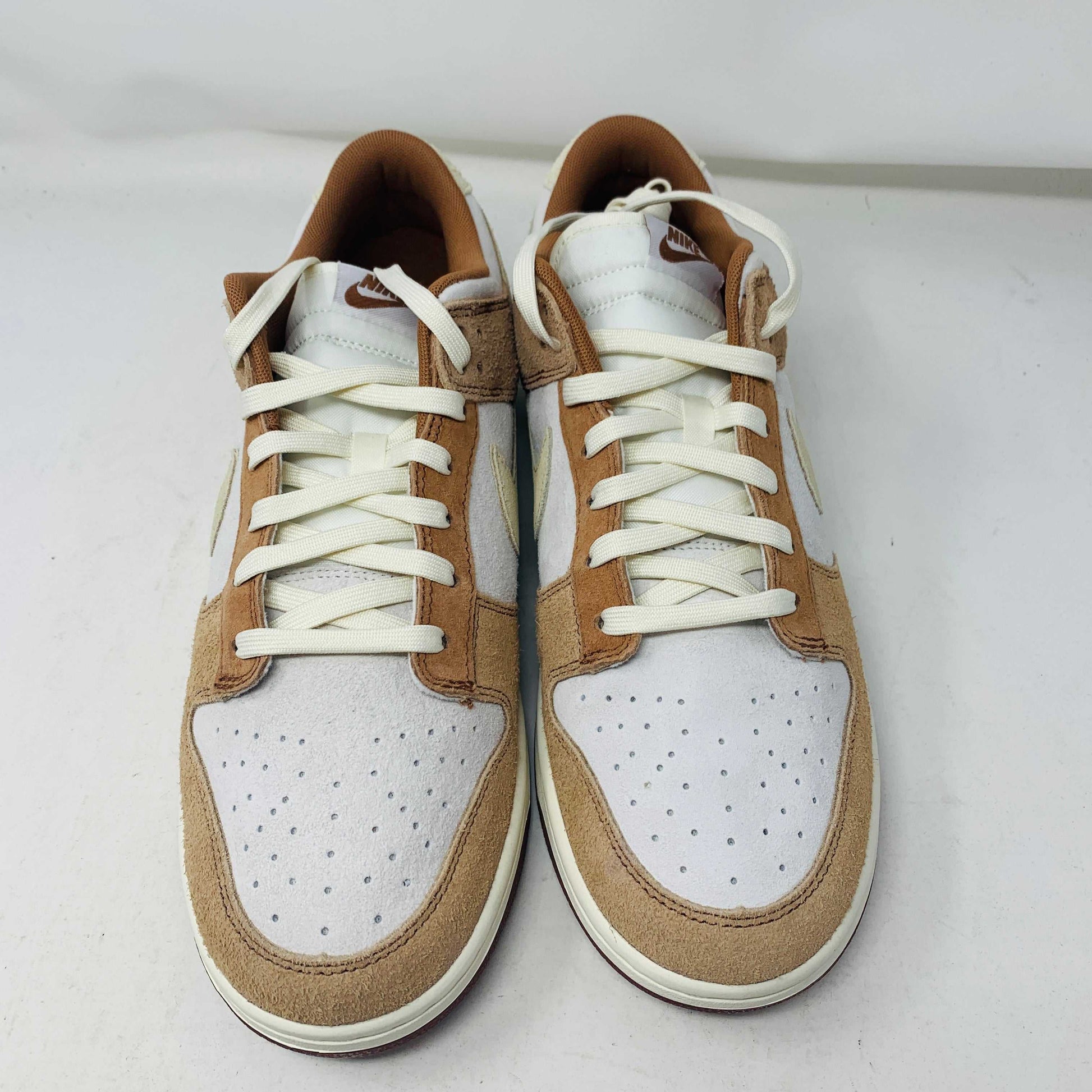 A brand new pair of Nike Dunk Low Medium Curry sneakers, with a beige suede upper and white swoosh accents, rests in pristine condition on a red box featuring the bold white Nike logo, set against a plain backdrop.