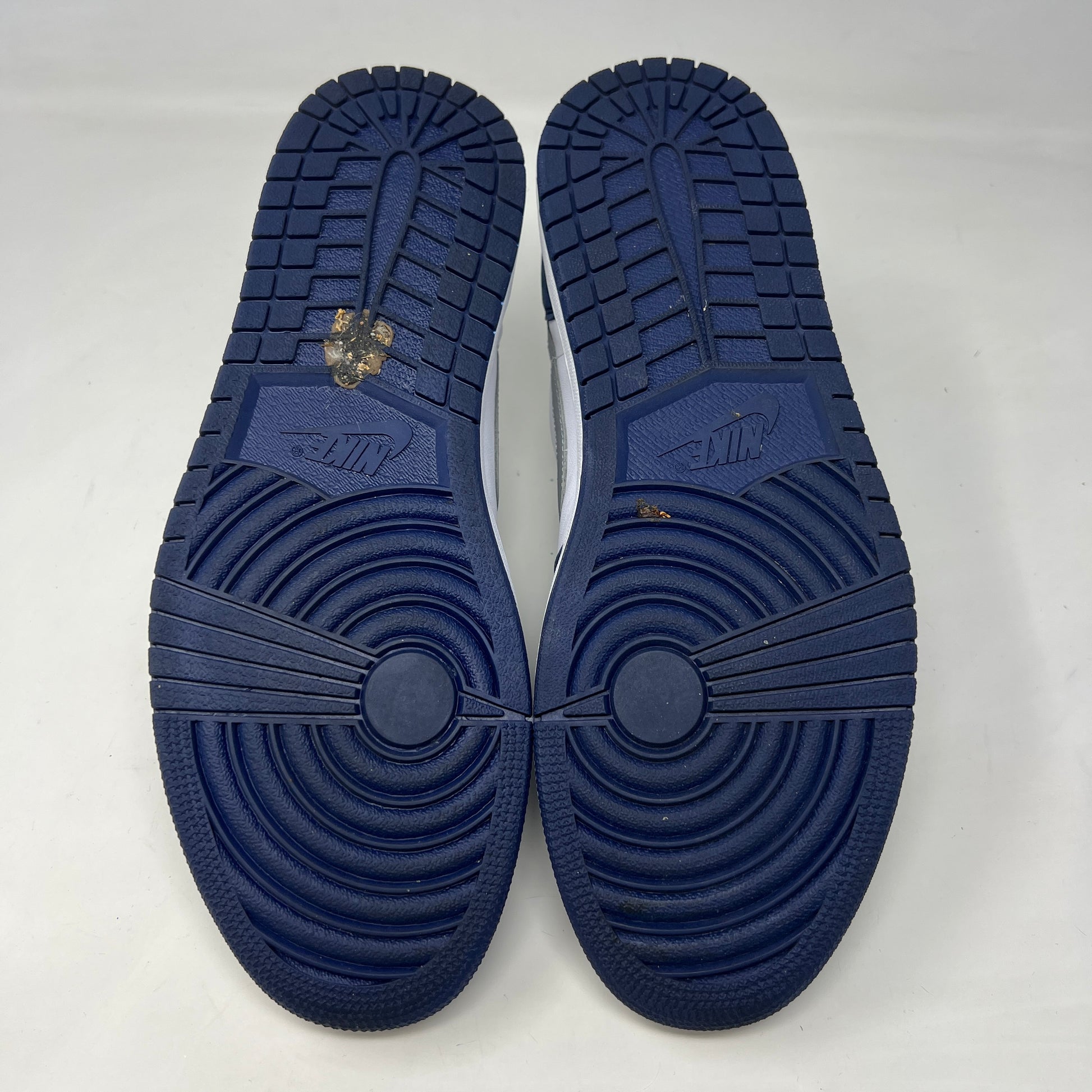 A Jordan 1 Low SB Midnight Navy shoe from Jordan, featuring blue toe and heel, white side panels, and a silver swoosh, is displayed on its box. The VERY CLEAN UPPERS are complemented by the size and product info visible on the label.