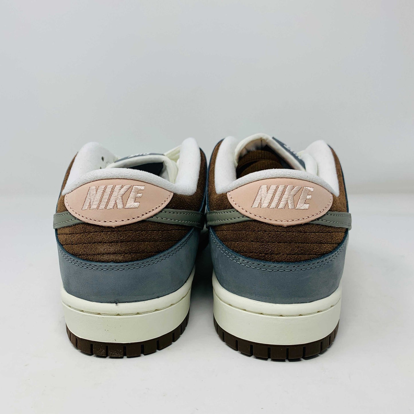The Nike SB Dunk Low Yuto Horigome sneaker, with a white and light blue design featuring a gray swoosh, is displayed on a white Nike SB box. The authentic shoe has pink and brown laces, a brown sole, and an embroidered logo on the heel.