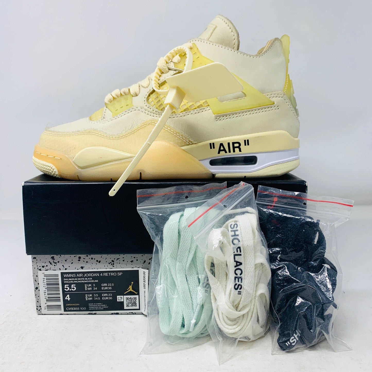 Jordan 4 Retro Off-White Sail Women's sneakers with cream, teal, and black laces, hangtag, and zip tie, shown in display.