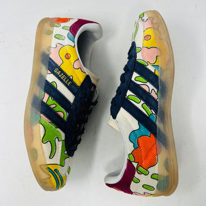The Adidas Gazelle Indoor Sean Wotherspoon sneaker, with colorful abstract uppers in yellow, red, pink, and green, dark blue stripes, red laces, and translucent soles, rests on a blue box showing size and product details.