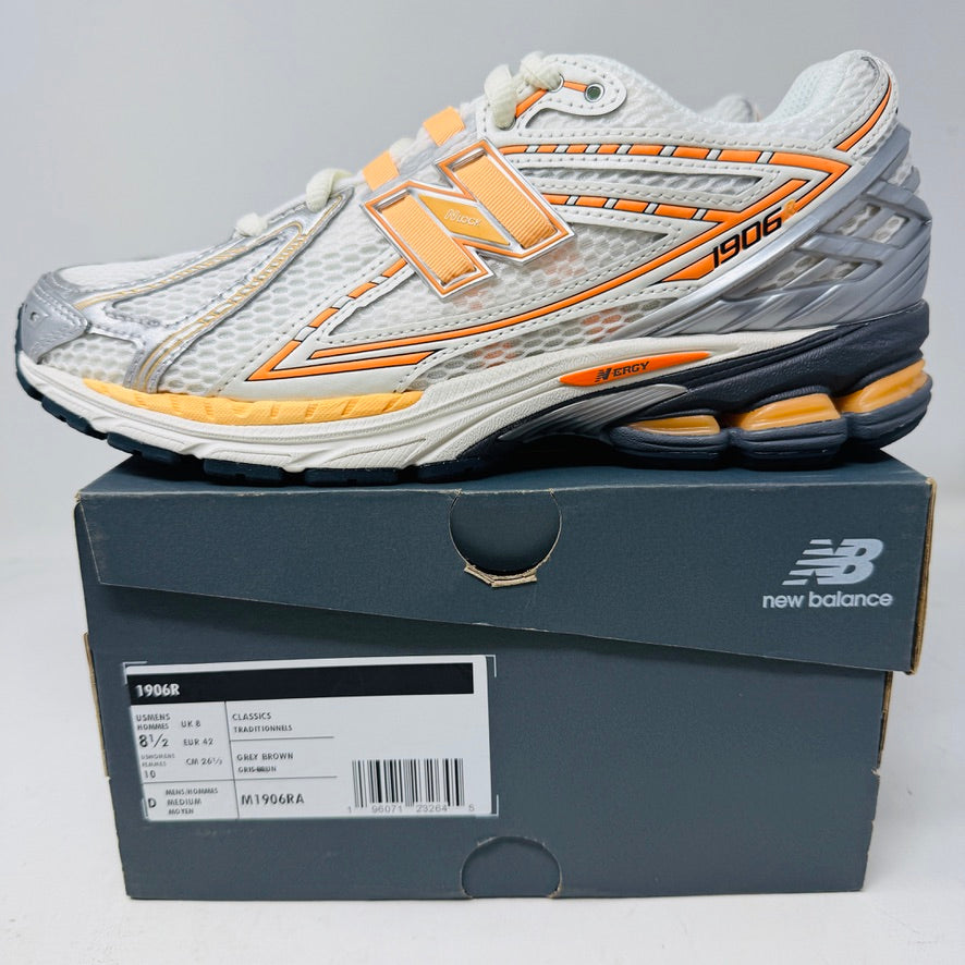 The New Balance 1906R ASOS Exclusive Neon Pack Orange sneakers feature intricate gray, white, orange, and yellow detailing with the iconic logo. Presented on a gray New Balance shoebox with size and model labels on the side, these sleek 2024 edition shoes are poised to elevate your style.