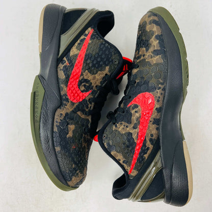 Close-up of a Nike Kobe 6 Protro Italian Camo (2024) (GS) shoe in black and dark olive with a red swoosh, resting on an orange Nike box. The 100% authentic shoe features a textured upper shown from the side, highlighting its design and striking color contrast.