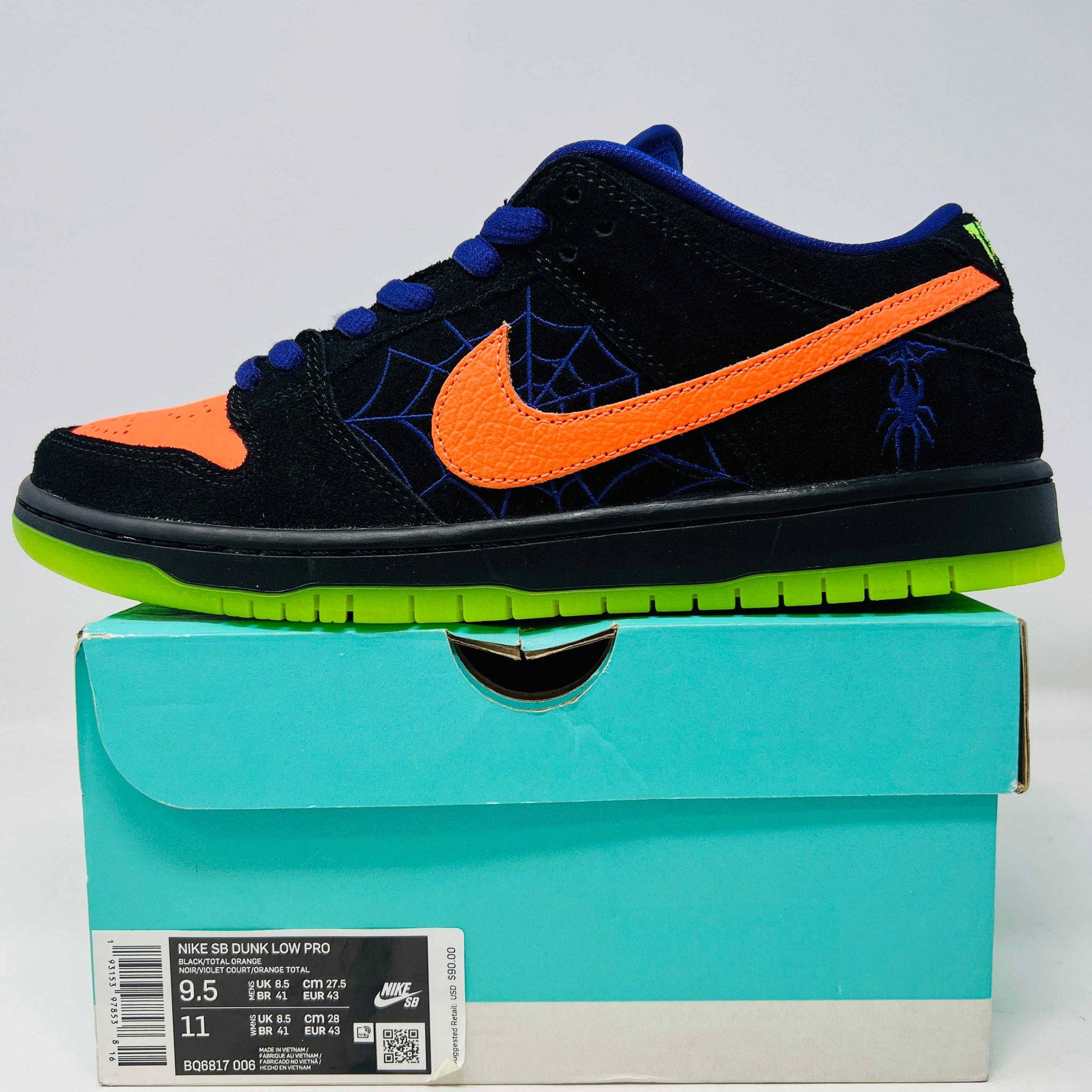 The Nike SB Dunk Low Night of Mischief sneakers feature Halloween-themed designs with orange swooshes, green soles, and spider web details. They come in a coffin-shaped box adorned with spooky jack-o-lanterns and webs, resting on a wooden floor.