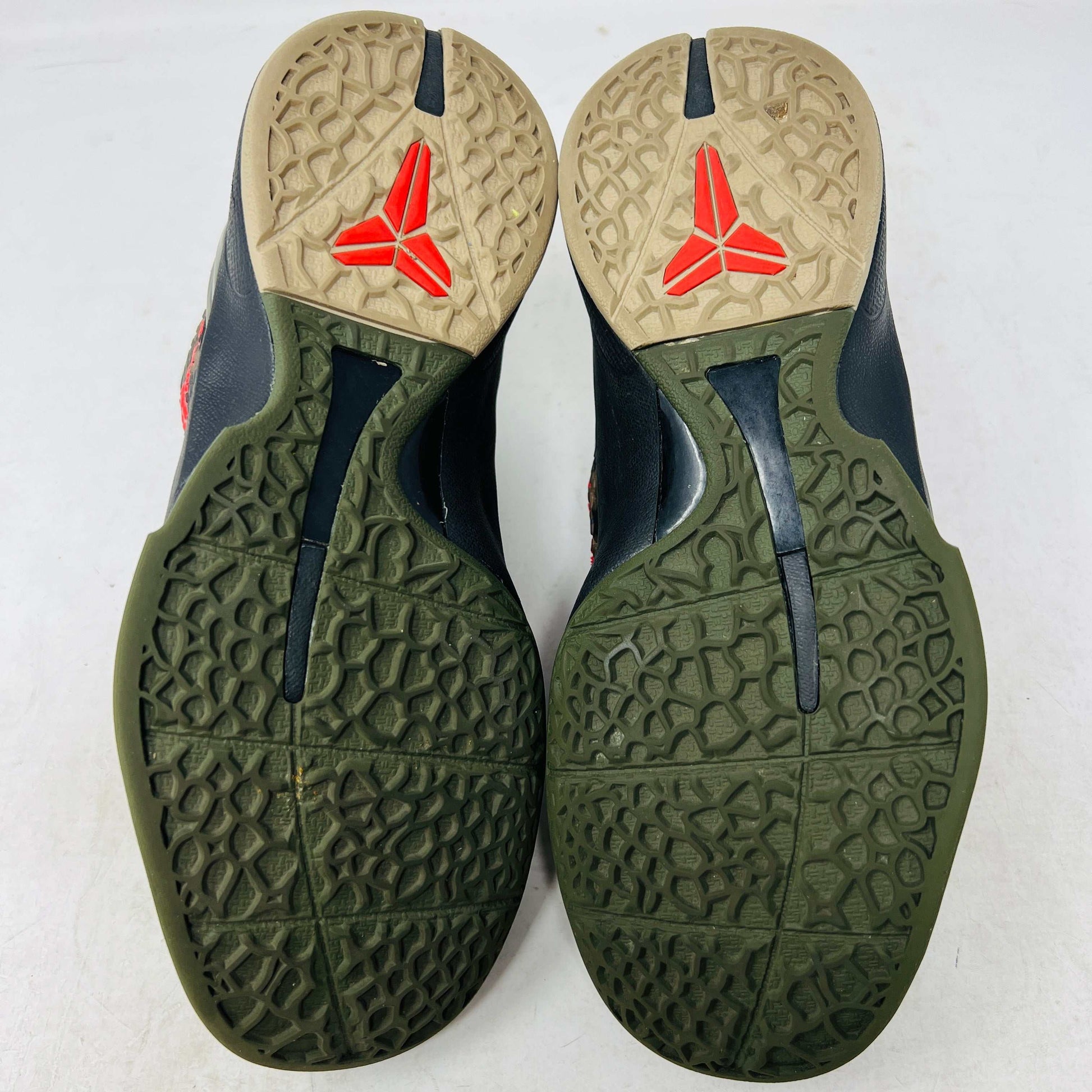 Close-up of a Nike Kobe 6 Protro Italian Camo (2024) (GS) shoe in black and dark olive with a red swoosh, resting on an orange Nike box. The 100% authentic shoe features a textured upper shown from the side, highlighting its design and striking color contrast.