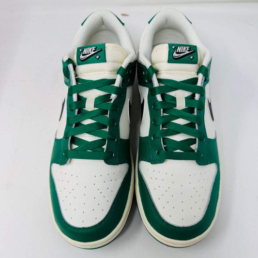 The Nike Dunk Low SE Lottery Pack Malachite Green sneaker, from the 2022 collection, is displayed on a red Nike shoebox. It features clean green and white uppers, a black swoosh logo, and a white midsole. The partially open lid shows essential shoe information and size labels.