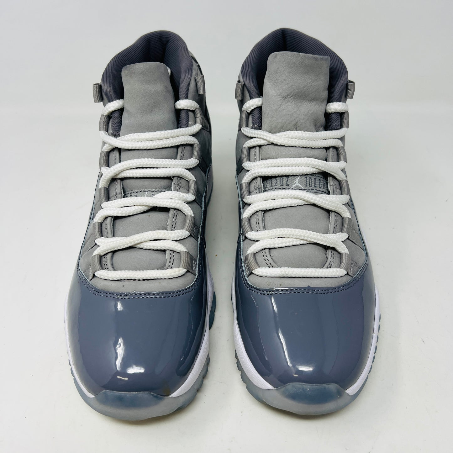The Jordan 11 Retro Cool Grey (2021) sneaker, featuring clean gray and white uppers with glossy patent leather accents and white laces, is displayed on a gray Nike Air shoebox. The shoe is authentic in size 9.5, with the box in good condition.