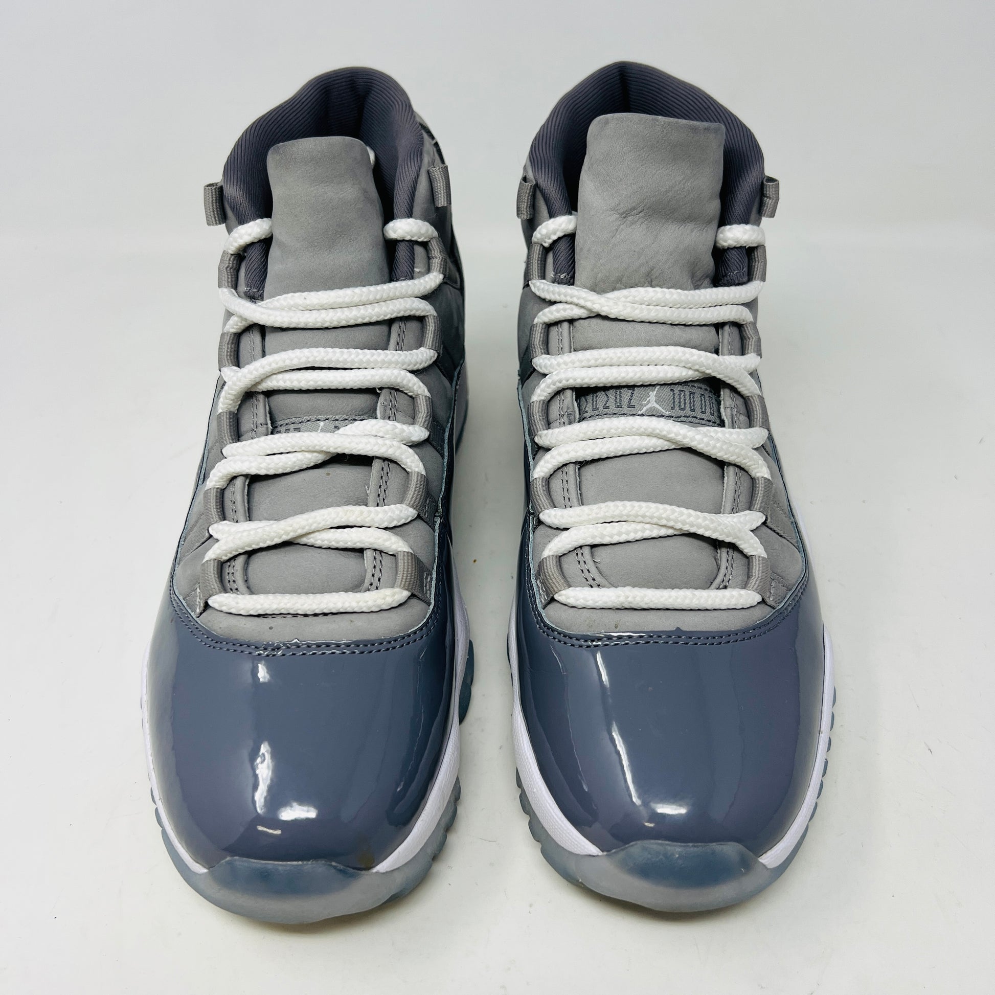The Jordan 11 Retro Cool Grey (2021) sneaker, featuring clean gray and white uppers with glossy patent leather accents and white laces, is displayed on a gray Nike Air shoebox. The shoe is authentic in size 9.5, with the box in good condition.