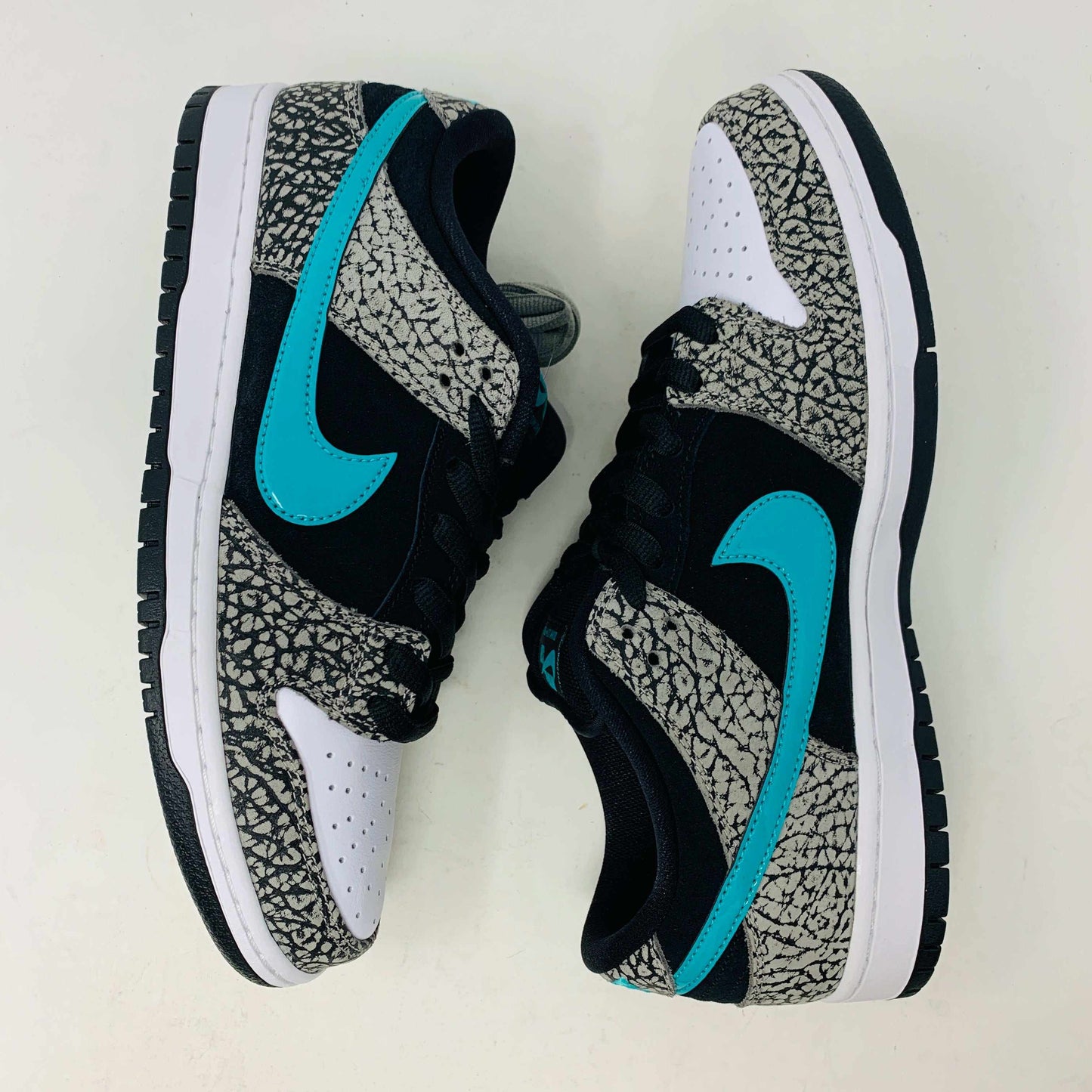 The Nike SB Dunk Low atmos Elephant sneakers feature a black and white textured pattern, teal Nike swoosh, and black laces, displayed on a purple Nike SB box with a white swoosh logo, ensuring 100% authenticity.