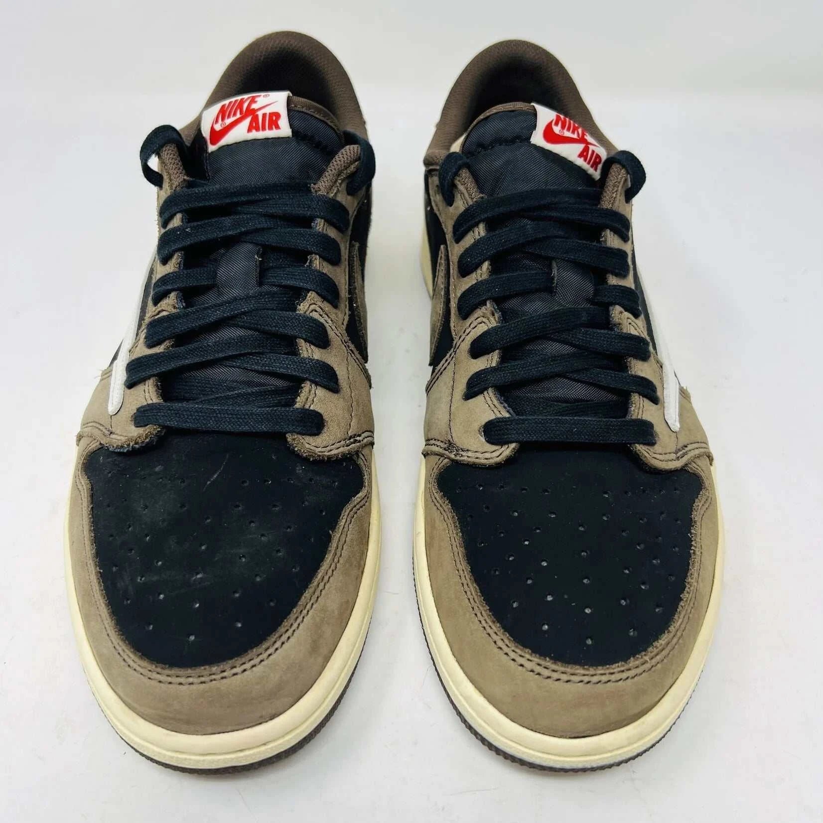 The Jordan 1 Retro Low OG SP Travis Scott Mocha sneakers, released in 2019 and featuring brown, black, and white tones, are displayed on a Nike box. Two extra lace sets, one red and one pink, are included in plastic bags beside the box.