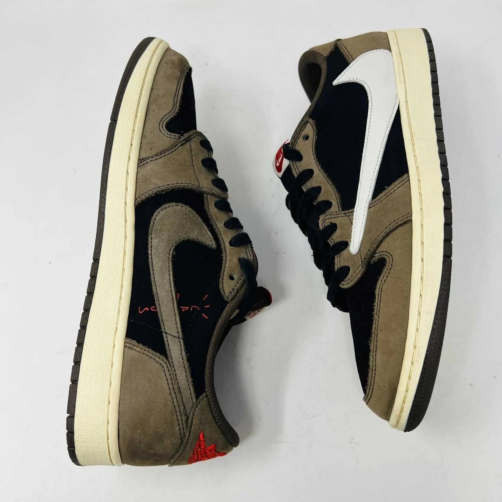 The Jordan 1 Retro Low OG SP Travis Scott Mocha sneakers, released in 2019 and featuring brown, black, and white tones, are displayed on a Nike box. Two extra lace sets, one red and one pink, are included in plastic bags beside the box.
