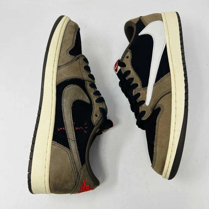 The Jordan 1 Retro Low OG SP Travis Scott Mocha sneakers, released in 2019 and featuring brown, black, and white tones, are displayed on a Nike box. Two extra lace sets, one red and one pink, are included in plastic bags beside the box.