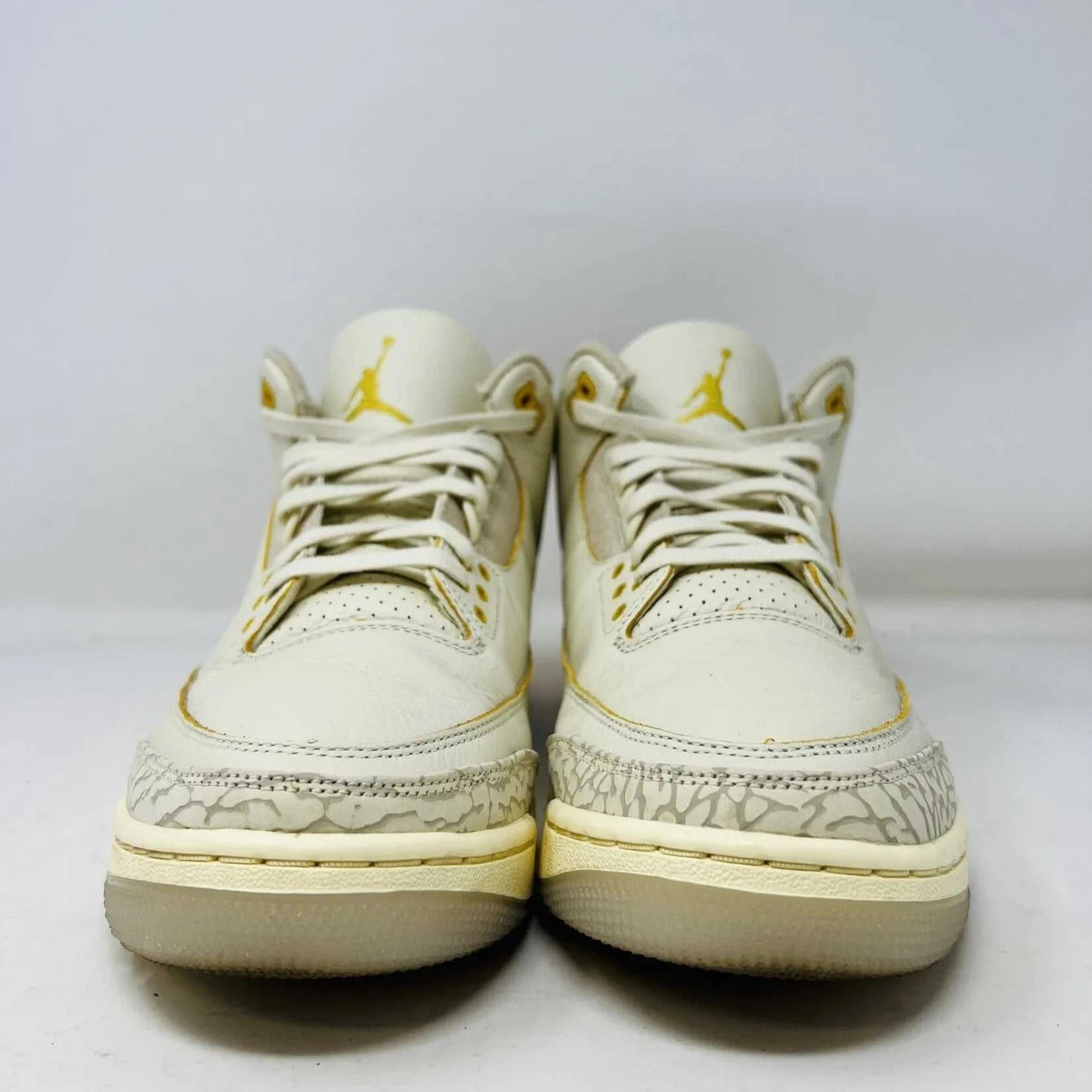 The Jordan 3 Retro SP J Balvin Medellín Sunset showcases clean cream uppers atop a shoebox with a gradient from yellow to dark red. A smiley face tag with lightning bolts confirms its 100% authenticity, highlighting this special 2023 release.