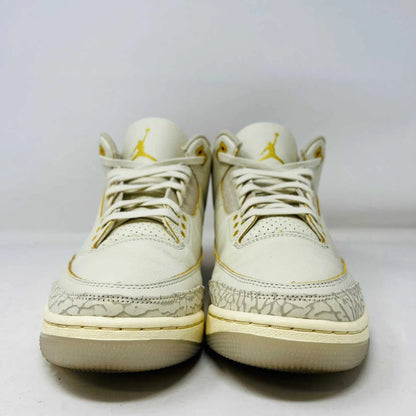 The Jordan 3 Retro SP J Balvin Medellín Sunset showcases clean cream uppers atop a shoebox with a gradient from yellow to dark red. A smiley face tag with lightning bolts confirms its 100% authenticity, highlighting this special 2023 release.