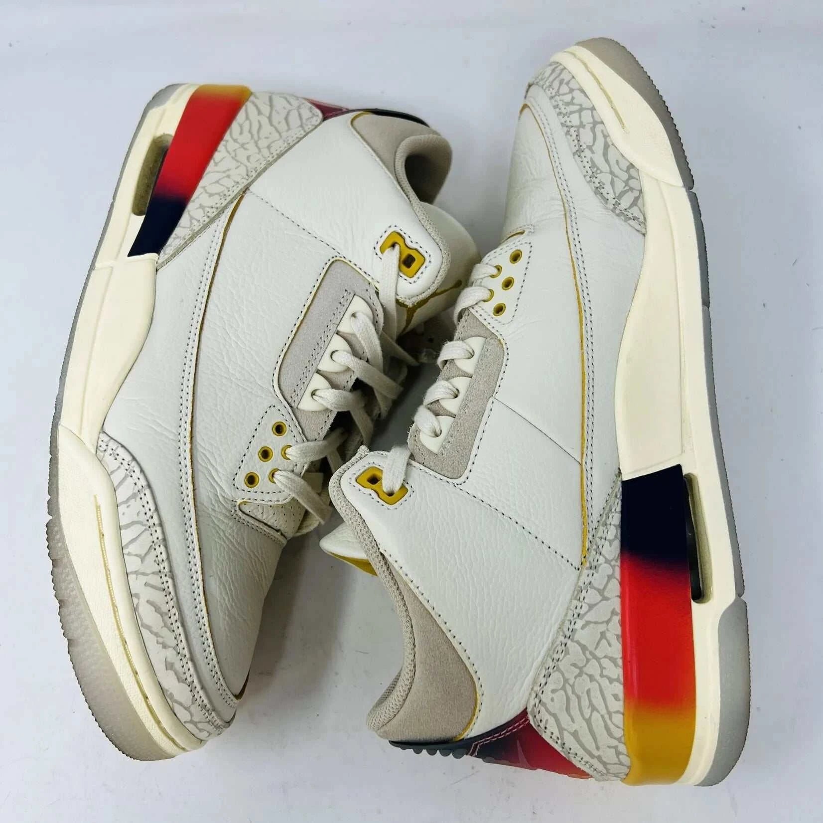 The Jordan 3 Retro SP J Balvin Medellín Sunset showcases clean cream uppers atop a shoebox with a gradient from yellow to dark red. A smiley face tag with lightning bolts confirms its 100% authenticity, highlighting this special 2023 release.