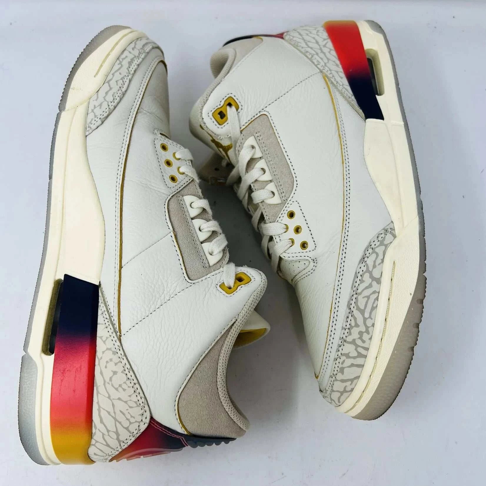 The Jordan 3 Retro SP J Balvin Medellín Sunset showcases clean cream uppers atop a shoebox with a gradient from yellow to dark red. A smiley face tag with lightning bolts confirms its 100% authenticity, highlighting this special 2023 release.