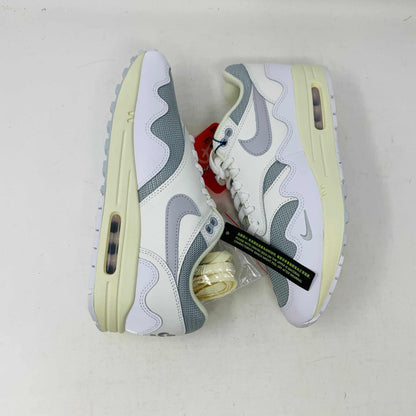 The Nike Air Max 1 Patta Waves White, a brand new sneaker, features a visible air cushion sole and swoosh logo. It comes elegantly displayed on a matching P.G.L.F.A. box with extra laces in a plastic bag attached to the tongue.