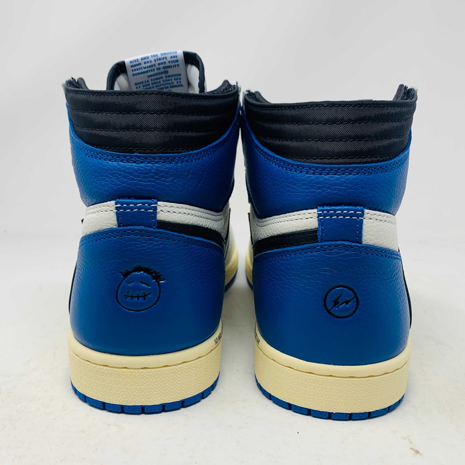 The Jordan 1 Retro High OG SP Fragment x Travis Scott is a new high-top sneaker featuring a blue, white, and black design with a unique backward Nike swoosh. It comes in a transparent, branded box adorned with butterfly and text details, boasting a thick sole and classic 1985 Air Jordan design.