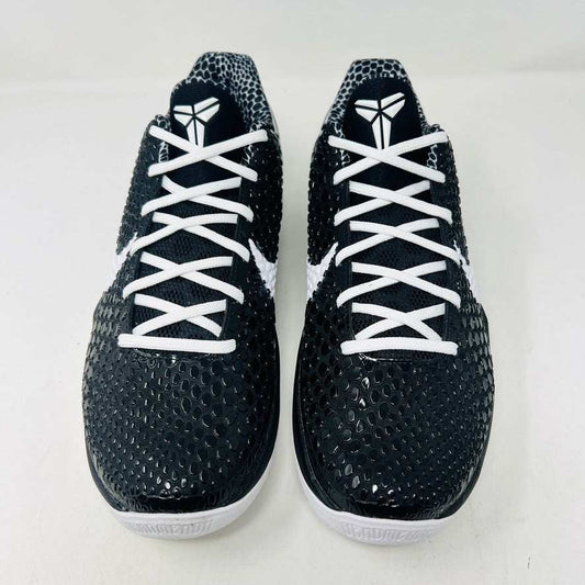 The KOBE Nike Kobe 6 Protro Mambacita Sweet 16 shoe, featuring clean black and white uppers, a white Swoosh, and a small gold 2 on the heel, is displayed on top of its black box with a Nike label. A sealed bag containing black laces accompanies the box for an authentic presentation.
