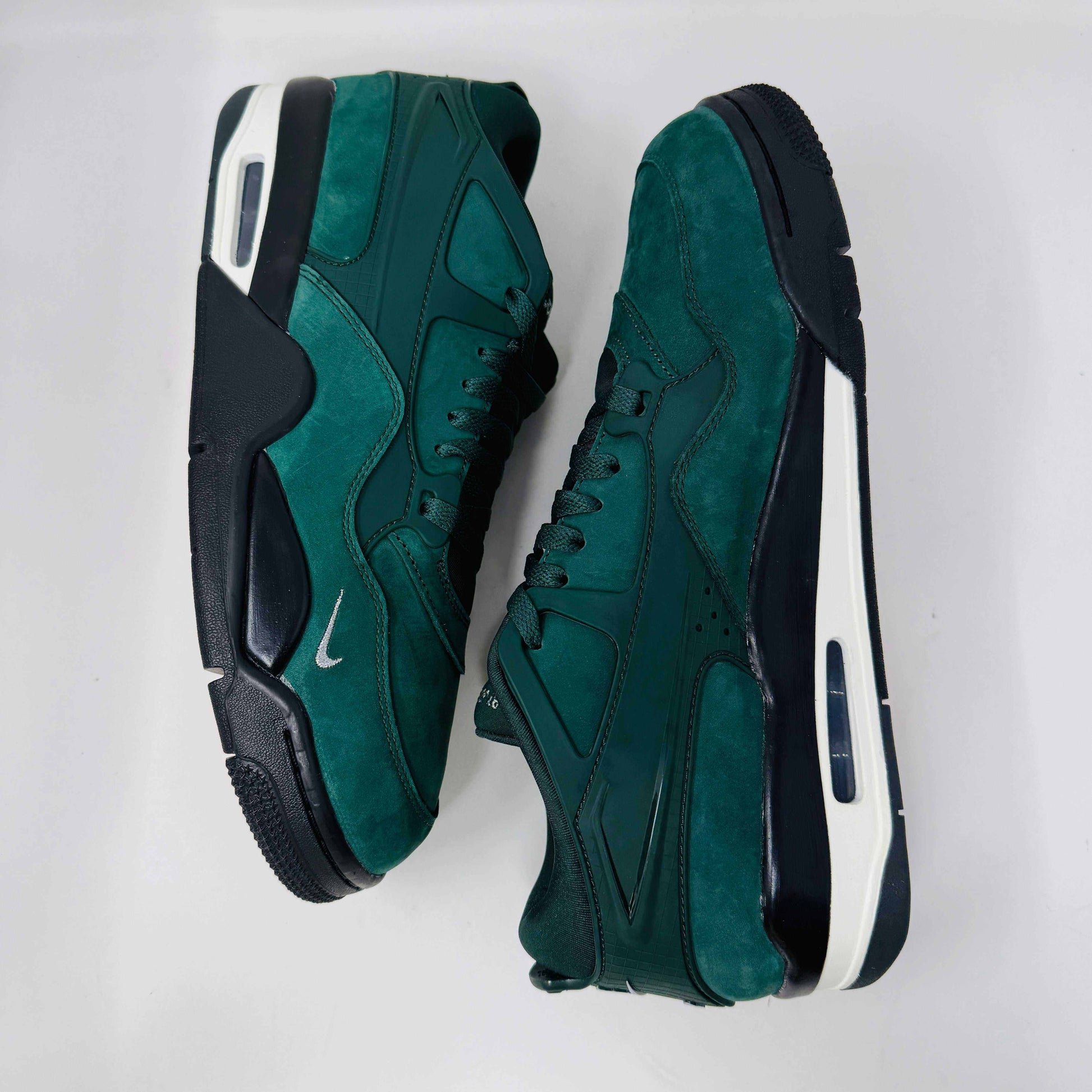The Jordan 4 RM SP Nigel Sylvester Grandmas Driveway sneakers feature a dark green color with Air by Jordan on the tongue in white, accented with white laces and a low-top design, all set against a plain white background.