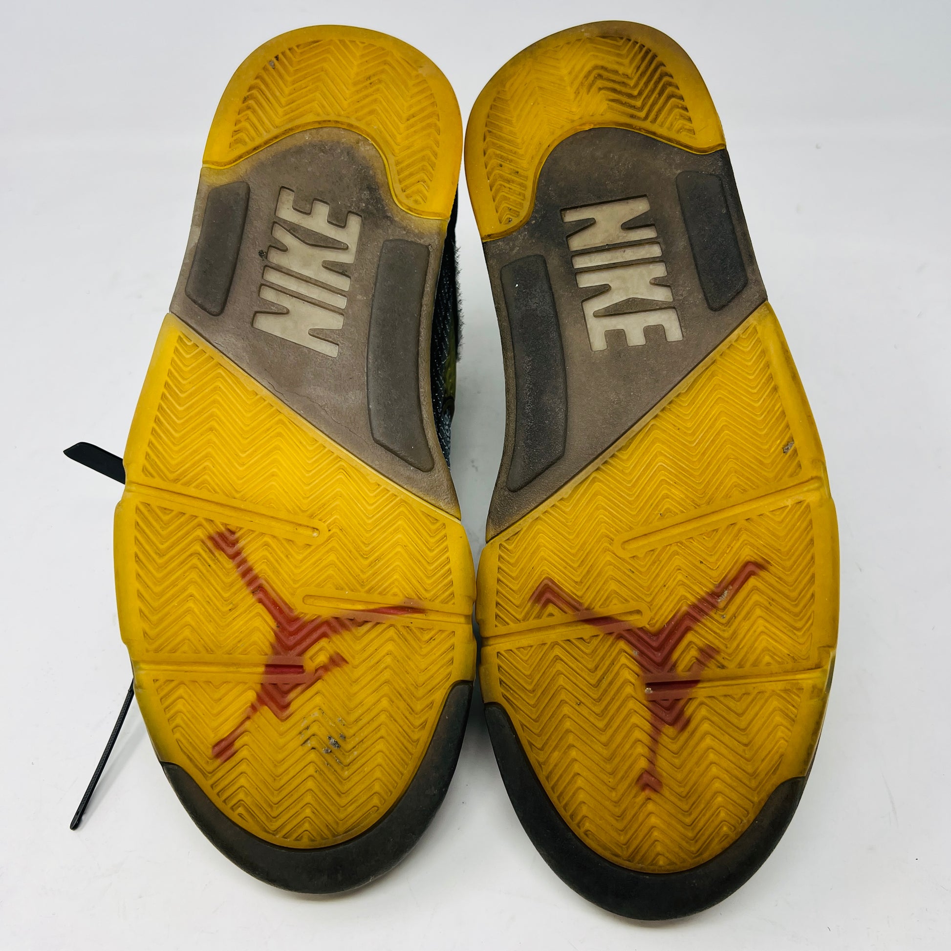 The Jordan 5 Retro Off-White Muslin high-top sneaker, featuring a transparent mesh window and 23 on the heel, is displayed on its box with a white and red shoelace packet in front. A small bleach stain adds unique character to the design.