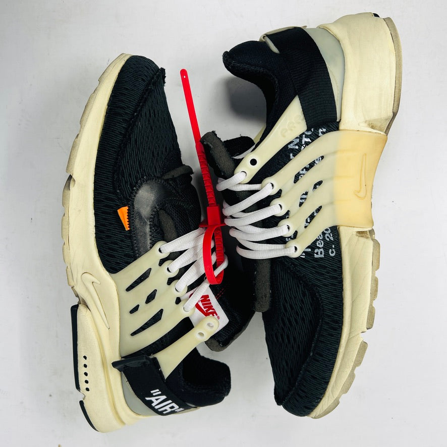 The 2017 classic Nike Air Presto Off-White features a black sneaker with white laces, a red tag, iconic AIR text, and an edgy zip tie. Displayed on its box, it includes extra black, neon green, and orange laces labeled SHOELACES.