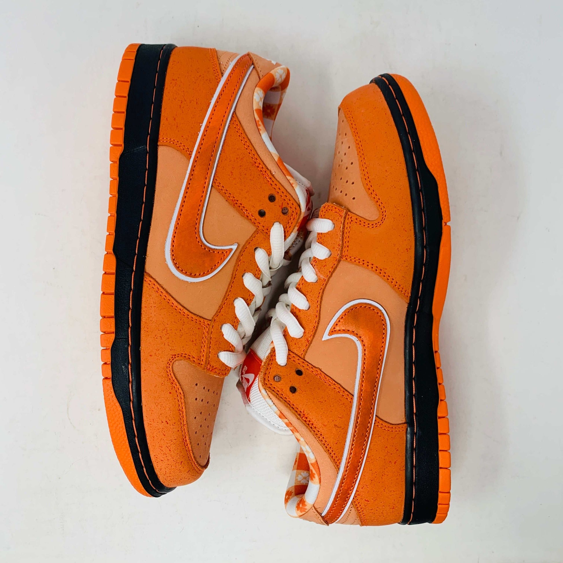 The authentic Nike SB Dunk Low Orange Lobster Concepts sneaker sits on a green and yellow Nike SB box. It features a white sole with black trim, an orange swoosh, and extra laces neatly positioned in front of the box.