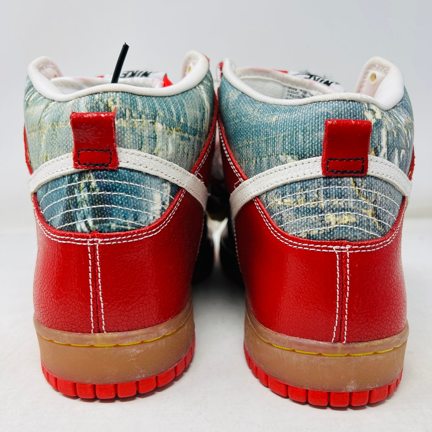 The Nike SB Dunk High Shoe Goo from 2008, priced at $525, sits atop its box. It features red and blue denim sections, a white swoosh, and a gum sole. A tag shows size and numbers, with extra laces beside the shoebox.