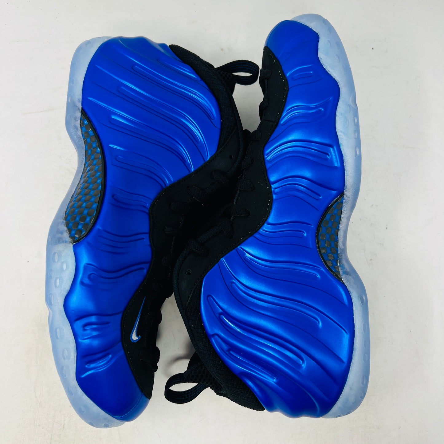 A brand-new Nike Air Foamposite One International Blue sneaker, featuring a striking blue upper with black accents, rests on a sleek black Nike shoebox. It has black mesh laces, a translucent sole with carbon fiber plate, and an iconic side swoosh.