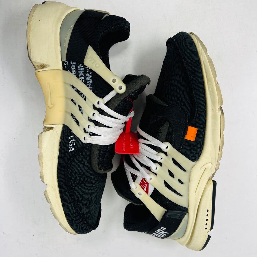 The 2017 classic Nike Air Presto Off-White features a black sneaker with white laces, a red tag, iconic AIR text, and an edgy zip tie. Displayed on its box, it includes extra black, neon green, and orange laces labeled SHOELACES.