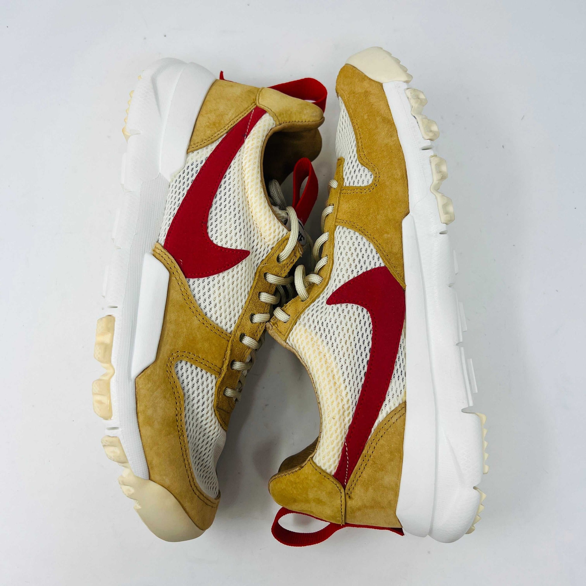 The NikeCraft Mars Yard Shoe 2.0 by Tom Sachs Space Camp features white mesh, tan suede accents, red Nike logos on the tongues, red heel pull tabs, and white laces. This 100% authentic sneaker is perfect for elevating any outfit with style.