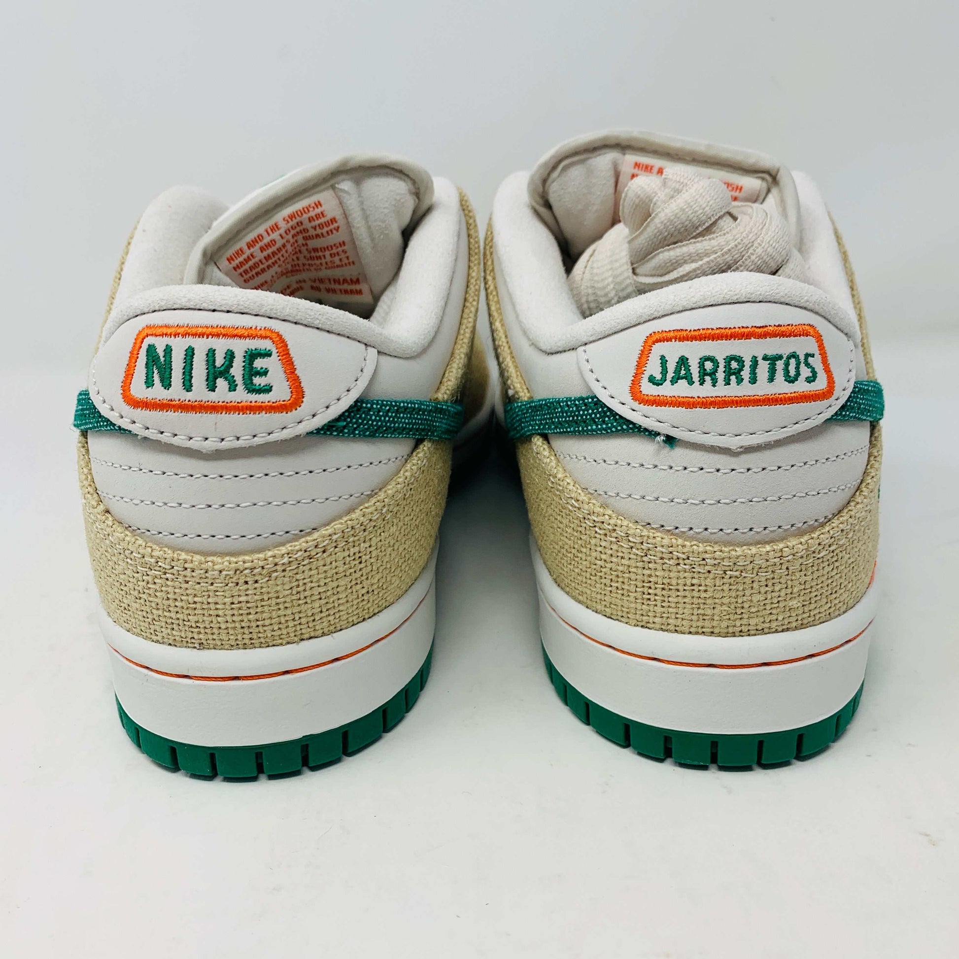 Front view of a brand new pair of Nike SB Dunk Low Jarritos sneakers in beige and white with green accents, featuring textured beige material, perforated toe panels, white laces, and swoosh logos on the tongues. Extra 2 laces included; displayed on a plain white background.