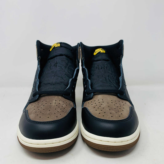 The Jordan 1 Retro High OG Palomino, a new black and brown sneaker from the Jordan brand, is displayed atop a pristine black and yellow Nike shoebox. The 2023 high-top design features the signature swoosh and Air Jordan logo, emphasizing its fresh-off-the-shelf allure.