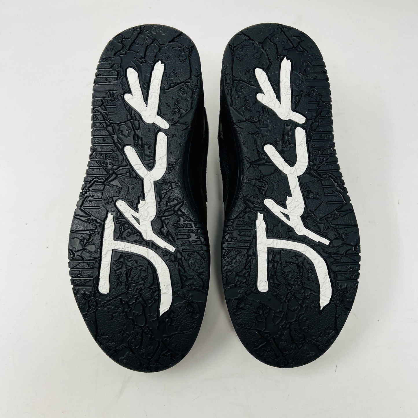 The image displays the soles of a pair of black Jordan Jumpman Jack TR Travis Scott Dark Mocha (PS) sneakers, featuring white, abstract, branch-like patterns against a plain white background that emphasizes the shoes unique design.