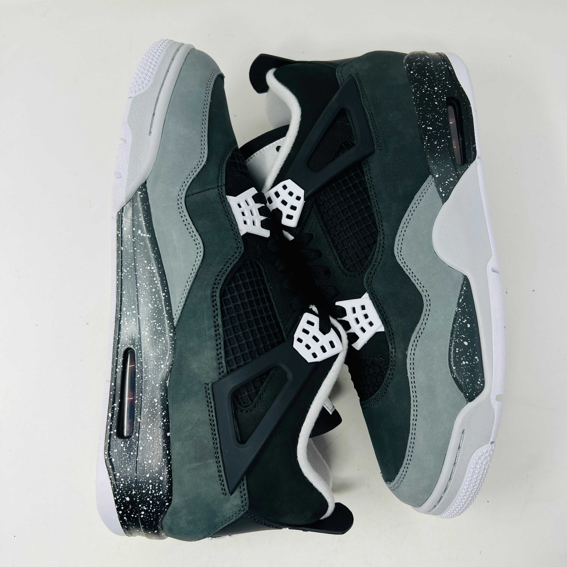 On top of a shoebox sits the brand-new Jordan 4 Retro Fear (2024), a stylish sneaker by Jordan. Its black and gray color scheme, black mesh accents, white midsole, and speckled heel details make it a must-have for 2024.