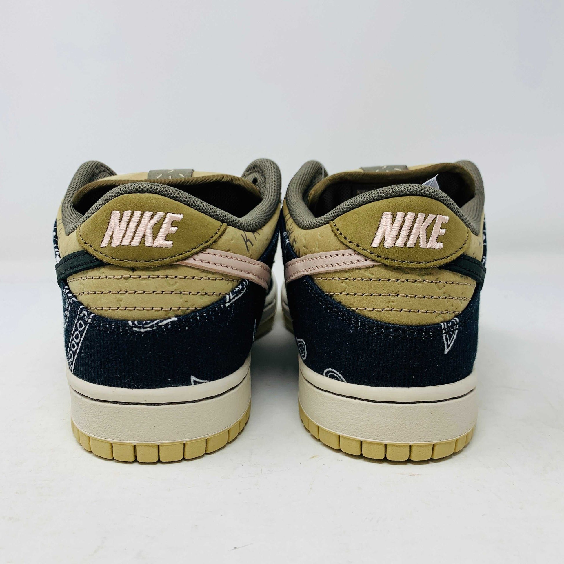 The Nike SB Dunk Low Travis Scott sneakers feature beige suede toe caps, black bandana-patterned overlays, white rope laces, authentic pink accents, and a brown label with text on the tongue. Brand new with extra laces, the interior is visible at the top.