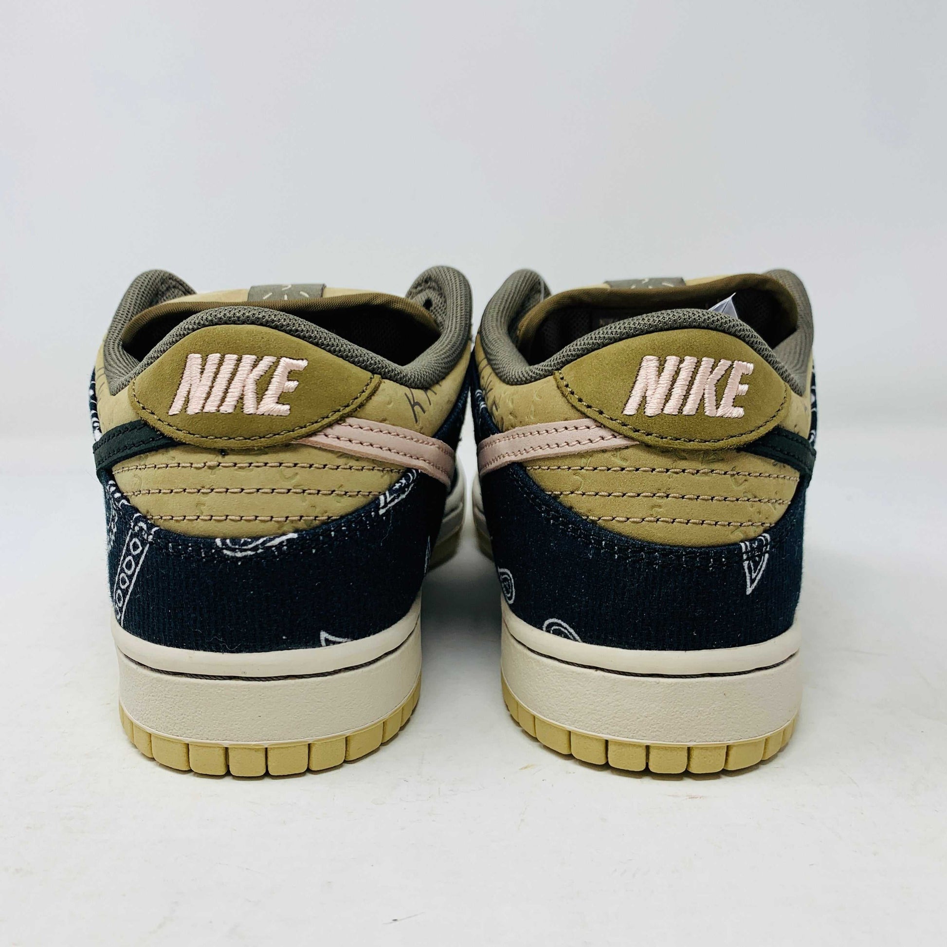 The Nike SB Dunk Low Travis Scott sneakers feature beige suede toe caps, black bandana-patterned overlays, white rope laces, authentic pink accents, and a brown label with text on the tongue. Brand new with extra laces, the interior is visible at the top.