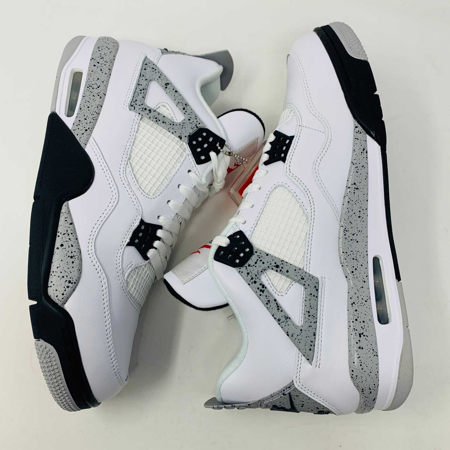 Check out the Jordan 4 White Cement 2016, a white sneaker with black and gray speckles. It features a small red jumping logo, comes in a matching box, and includes the classic 2016 Jordan hang tag for authenticity.