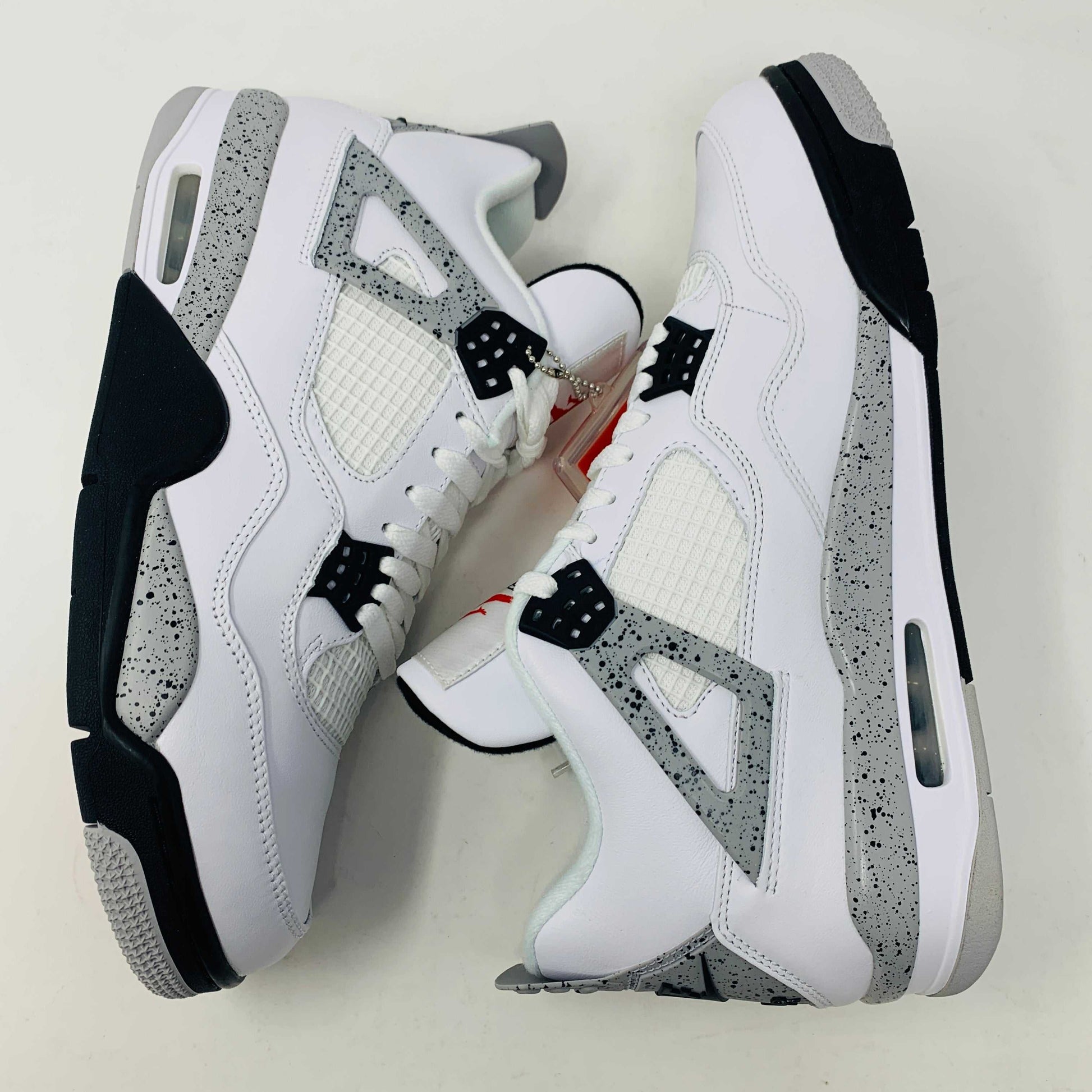 Check out the Jordan 4 White Cement 2016, a white sneaker with black and gray speckles. It features a small red jumping logo, comes in a matching box, and includes the classic 2016 Jordan hang tag for authenticity.