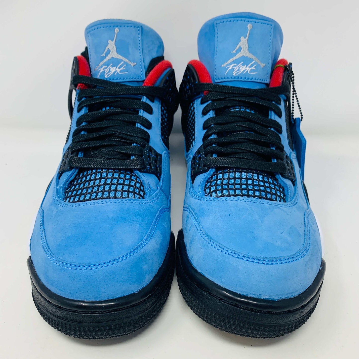 The Jordan 4 Retro Travis Scott Cactus Jack sneaker in blue, accented with black and red, features a visible air unit in the heel and a Jumpman logo hang tag, packaged in a black speckled box with an orange Jumpman logo and AIR.