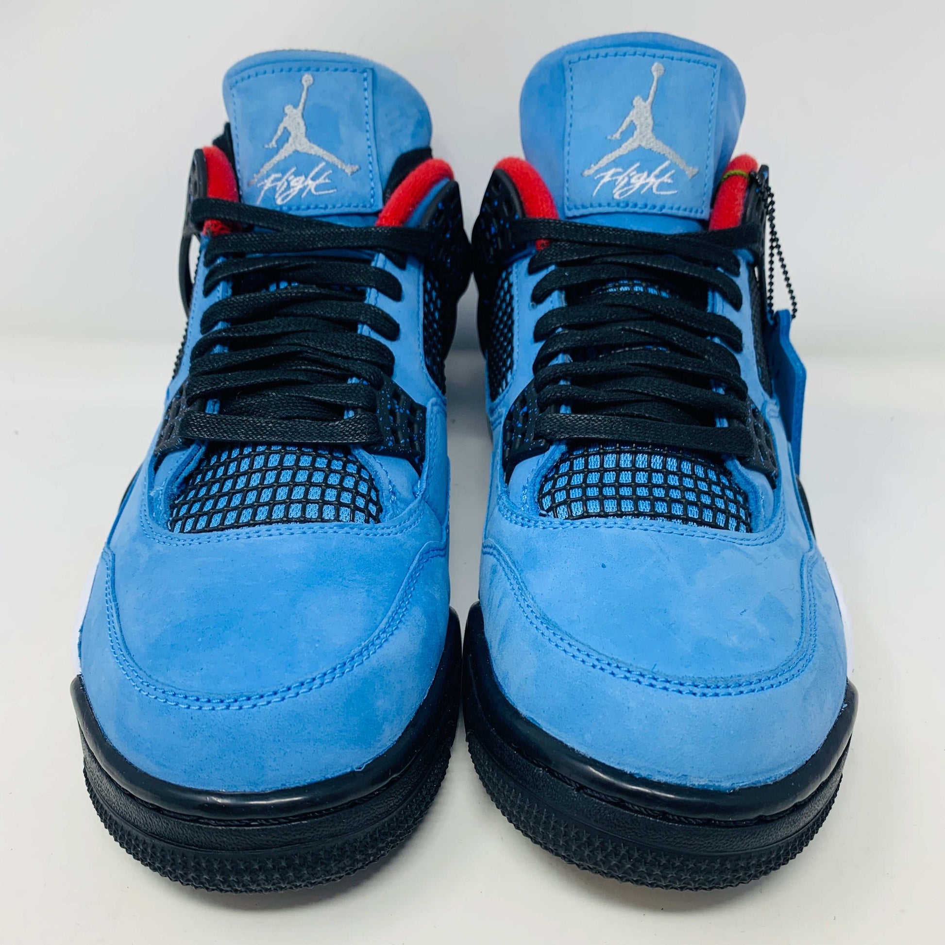 The Jordan 4 Retro Travis Scott Cactus Jack sneaker in blue, accented with black and red, features a visible air unit in the heel and a Jumpman logo hang tag, packaged in a black speckled box with an orange Jumpman logo and AIR.