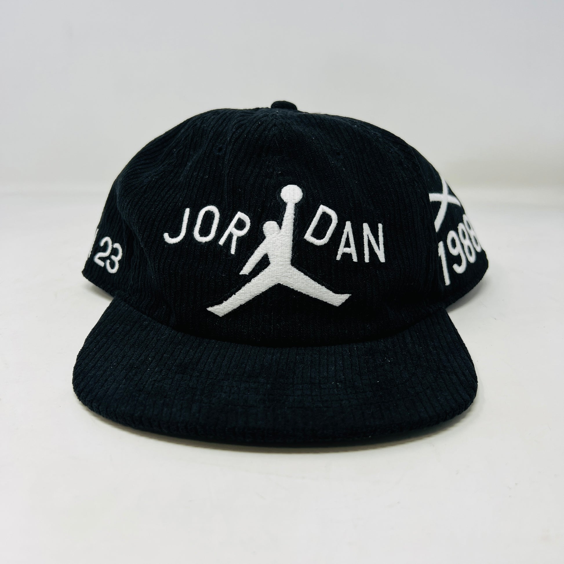 The Jordan x Nina Chanel Abney Club Cap Black features a sleek design with a stylized basketball player logo and JORDAN in white, the number 23 on the left, and 1988 on the right. It boasts a classic flat brim style.