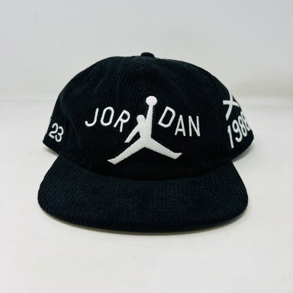 The Jordan x Nina Chanel Abney Club Cap Black features a sleek design with a stylized basketball player logo and JORDAN in white, the number 23 on the left, and 1988 on the right. It boasts a classic flat brim style.