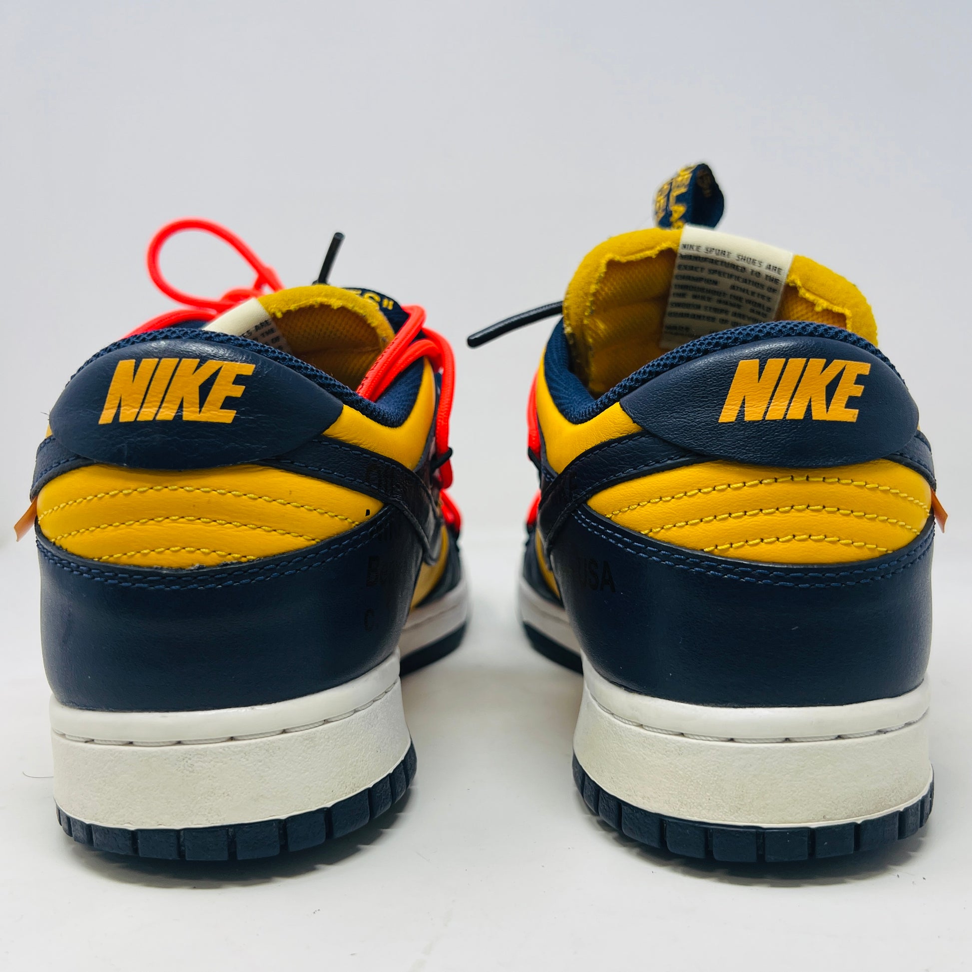 The 2019 Nike Dunk Low Off-White University Gold sneakers feature a navy and yellow design, accented with bold red laces and attached white tags and a zip tie. Displayed atop their box, the label lists them as US size 10.5 and UK size 12, all set against a plain white background.
