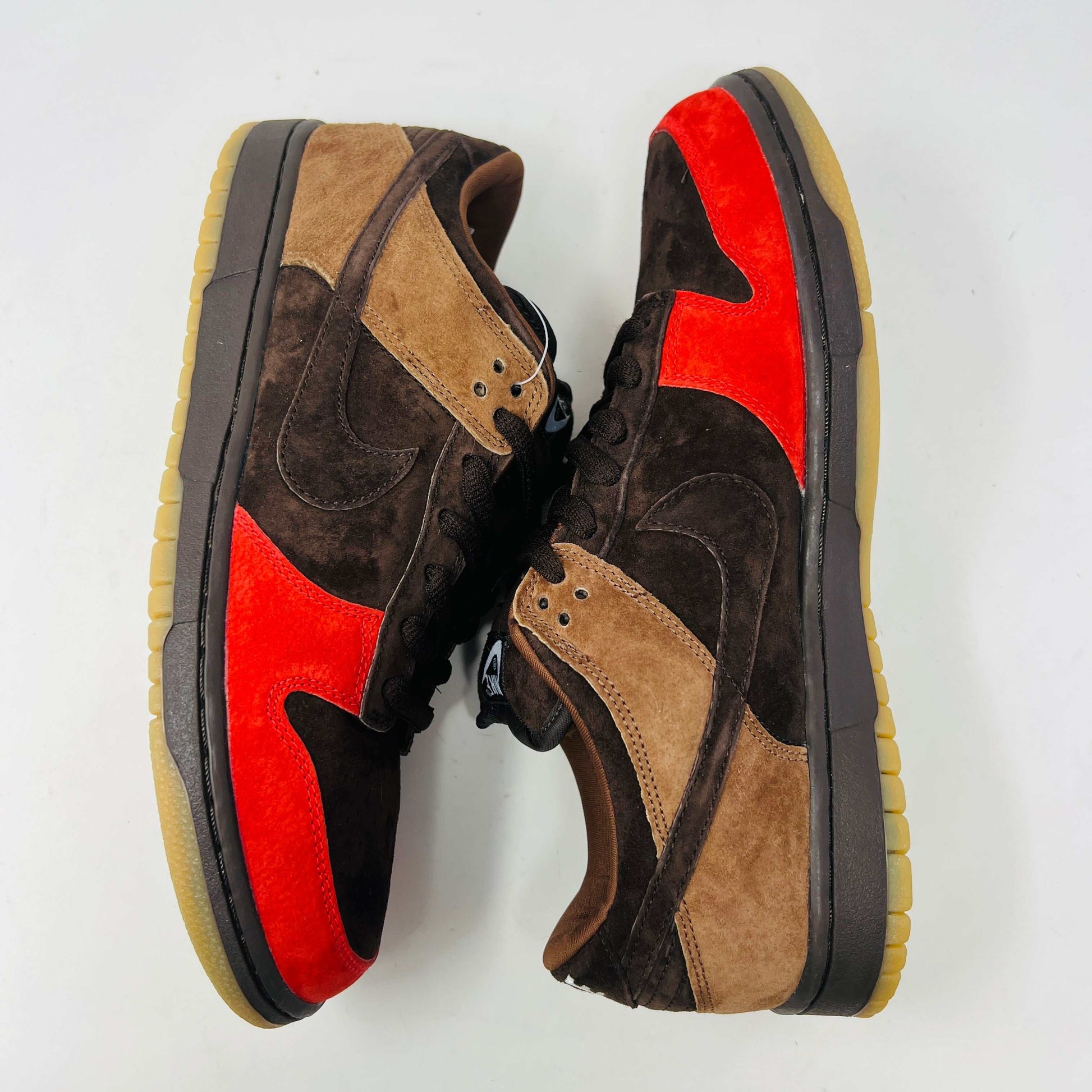 A pair of BRAND NEW Nike SB Dunk Low Bison sneakers featuring brown and red suede uppers, black laces, EXTRA LACES included, and a light brown sole. Positioned side by side on a white background, they promise to be 100% authentic and stylish.